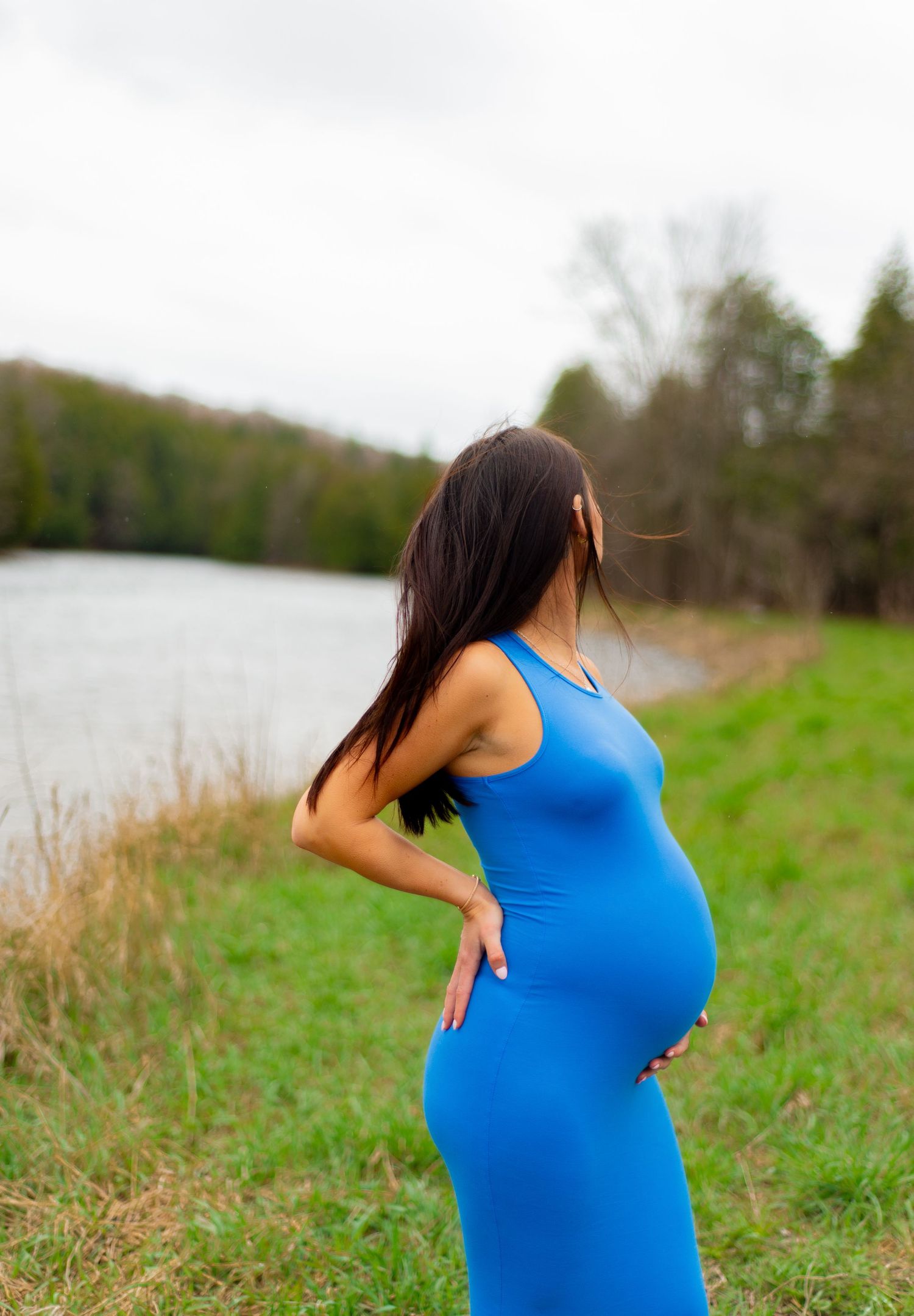 A side view maternity portrait in a blue dress by a peaceful river.