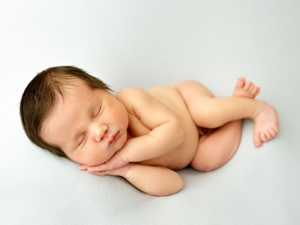 Sleeping newborn baby curled up peacefully on soft white backdrop in minimalist photography style.