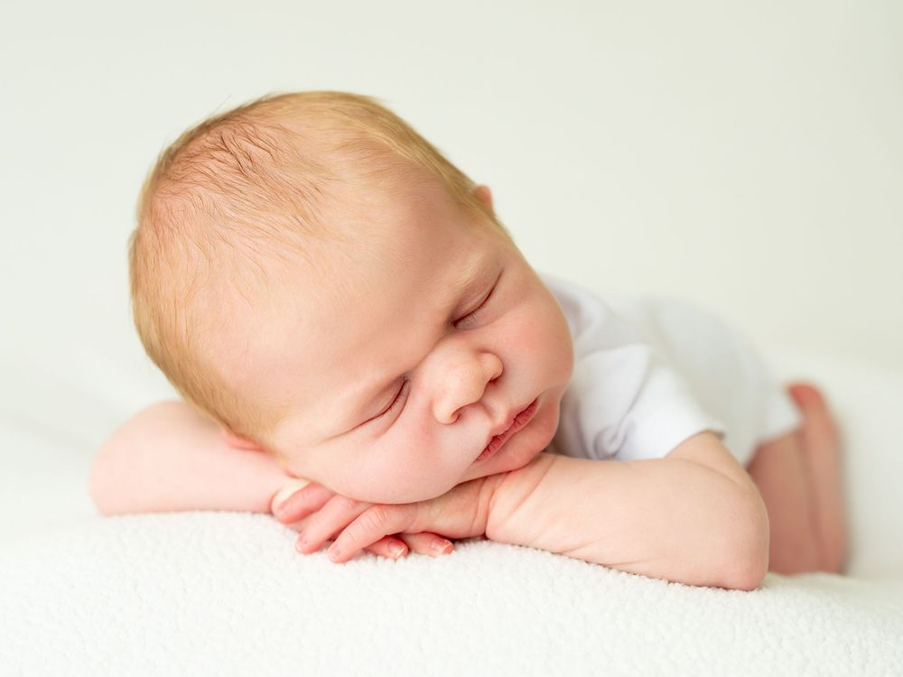 A sleeping baby rests peacefully on a white blanket with soft lighting creating a serene newborn portrait.