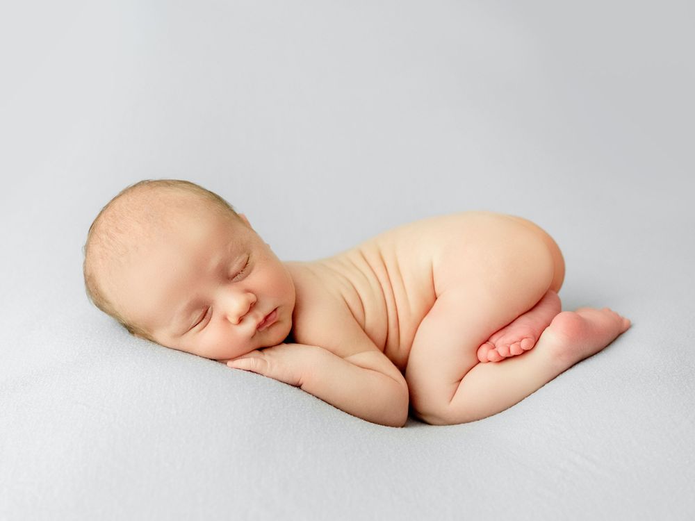 Peaceful sleeping newborn baby curled up on soft gray background in artistic portrait pose.
