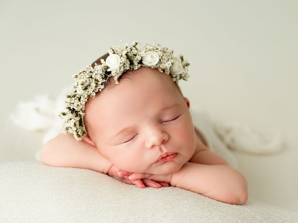 Sleeping newborn wearing delicate white floral crown in soft natural light portrait.