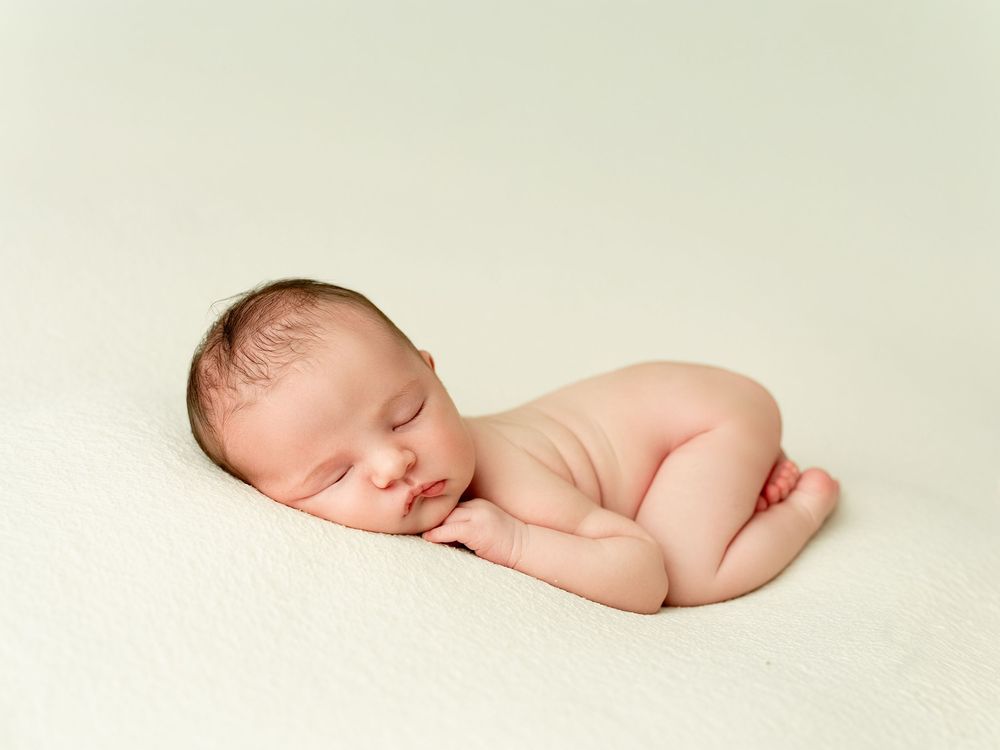 Peaceful sleeping newborn resting on cream backdrop in minimalist studio portrait.
