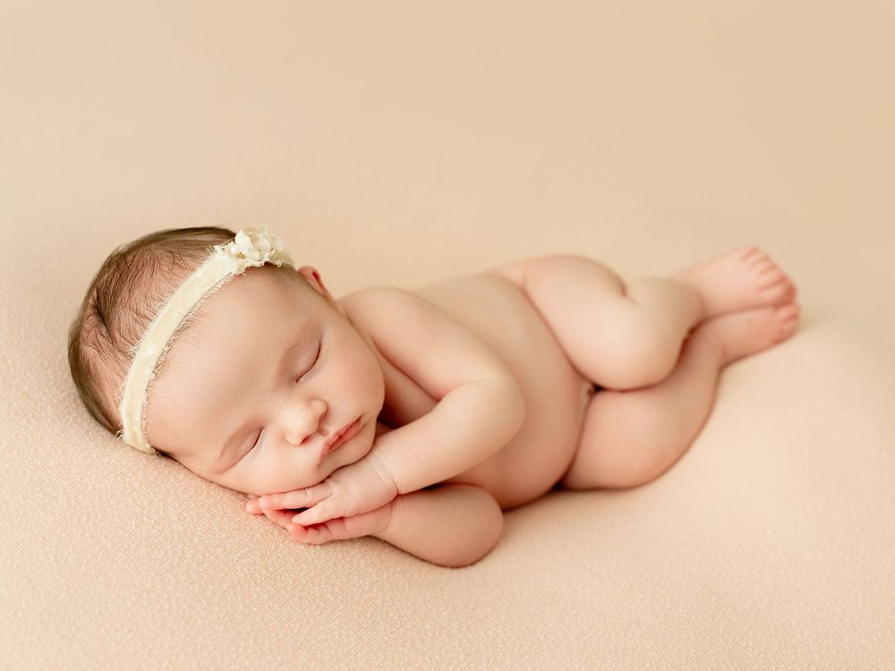 A sleeping newborn baby lies peacefully on a soft beige blanket in a minimalist photography setting.