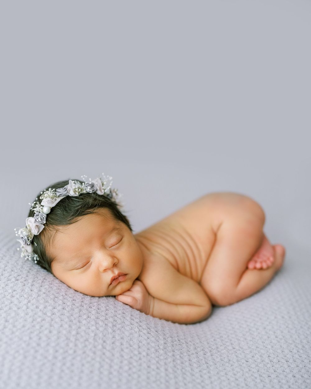 A sleeping newborn baby lies peacefully on a textured white blanket.