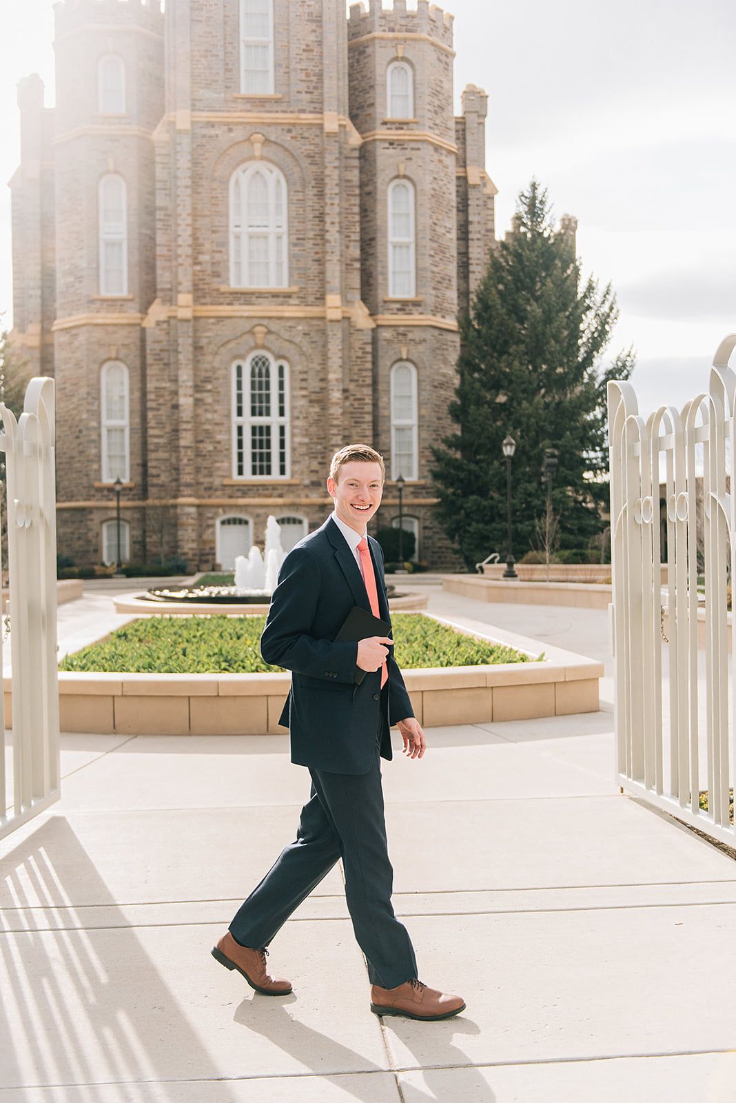 Professional in a navy suit and coral tie walking on a pathway in front of a grand historic church building.