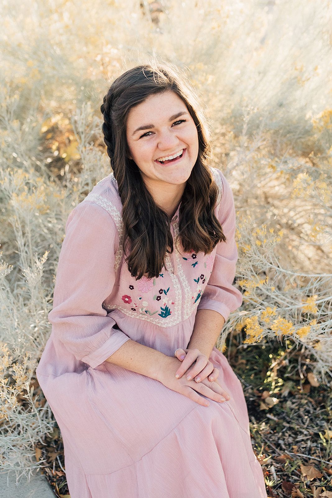 Portrait of someone in a pink dress sitting outdoors among autumn foliage.