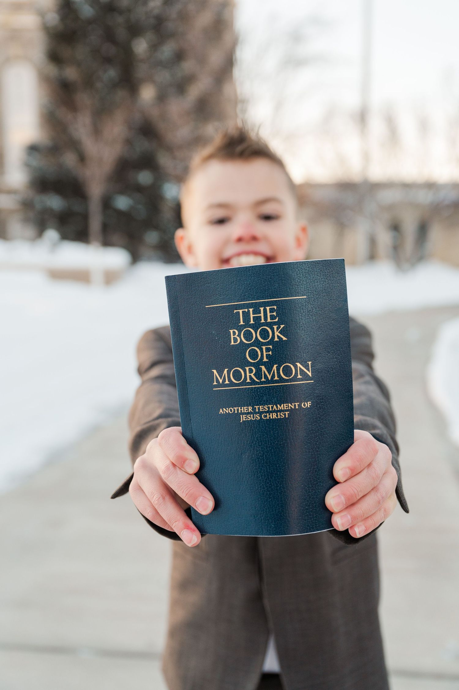Child holding up Book of Mormon with snow covered ground in background.