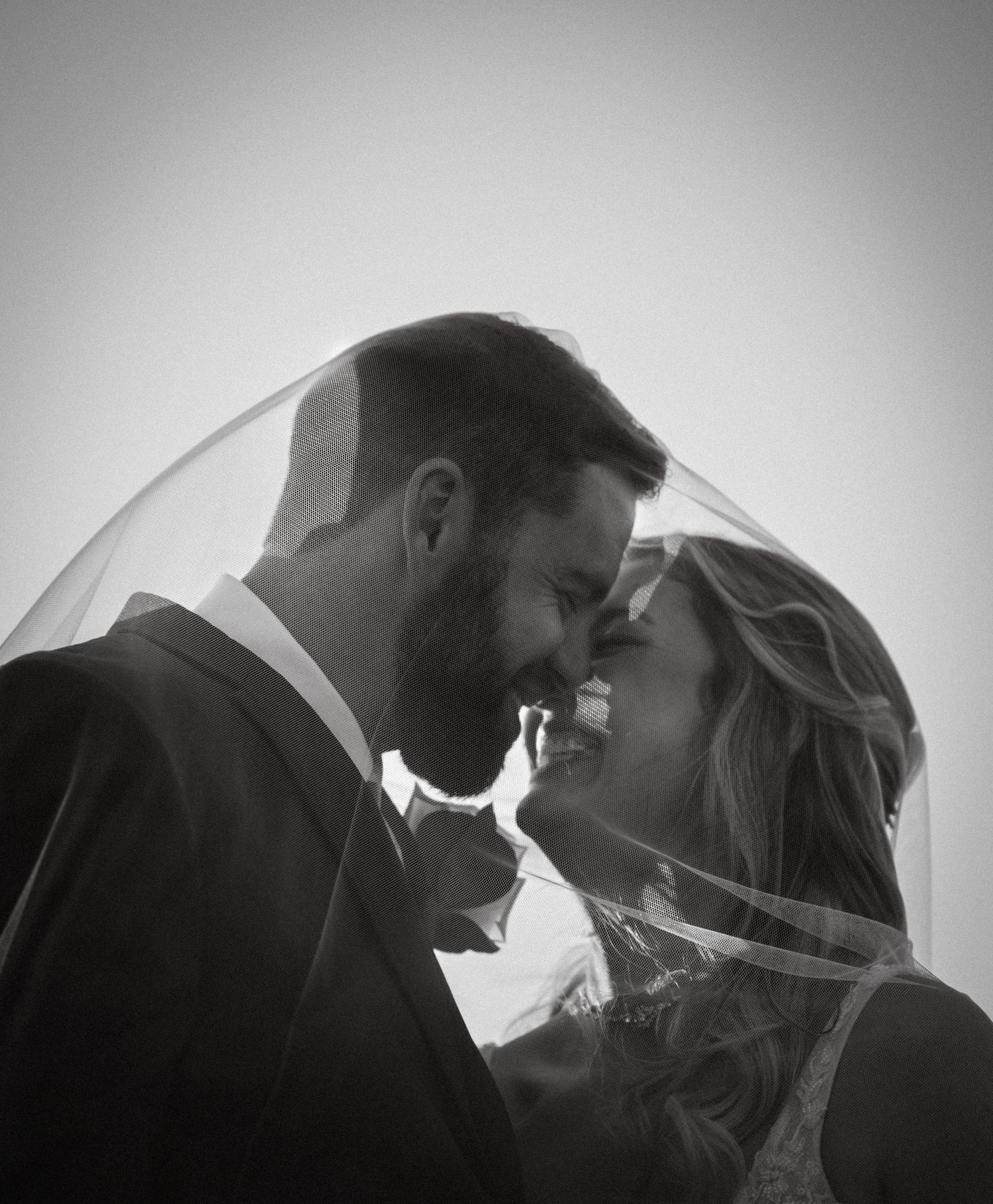 Intimate black and white portrait of newlyweds under wedding veil.