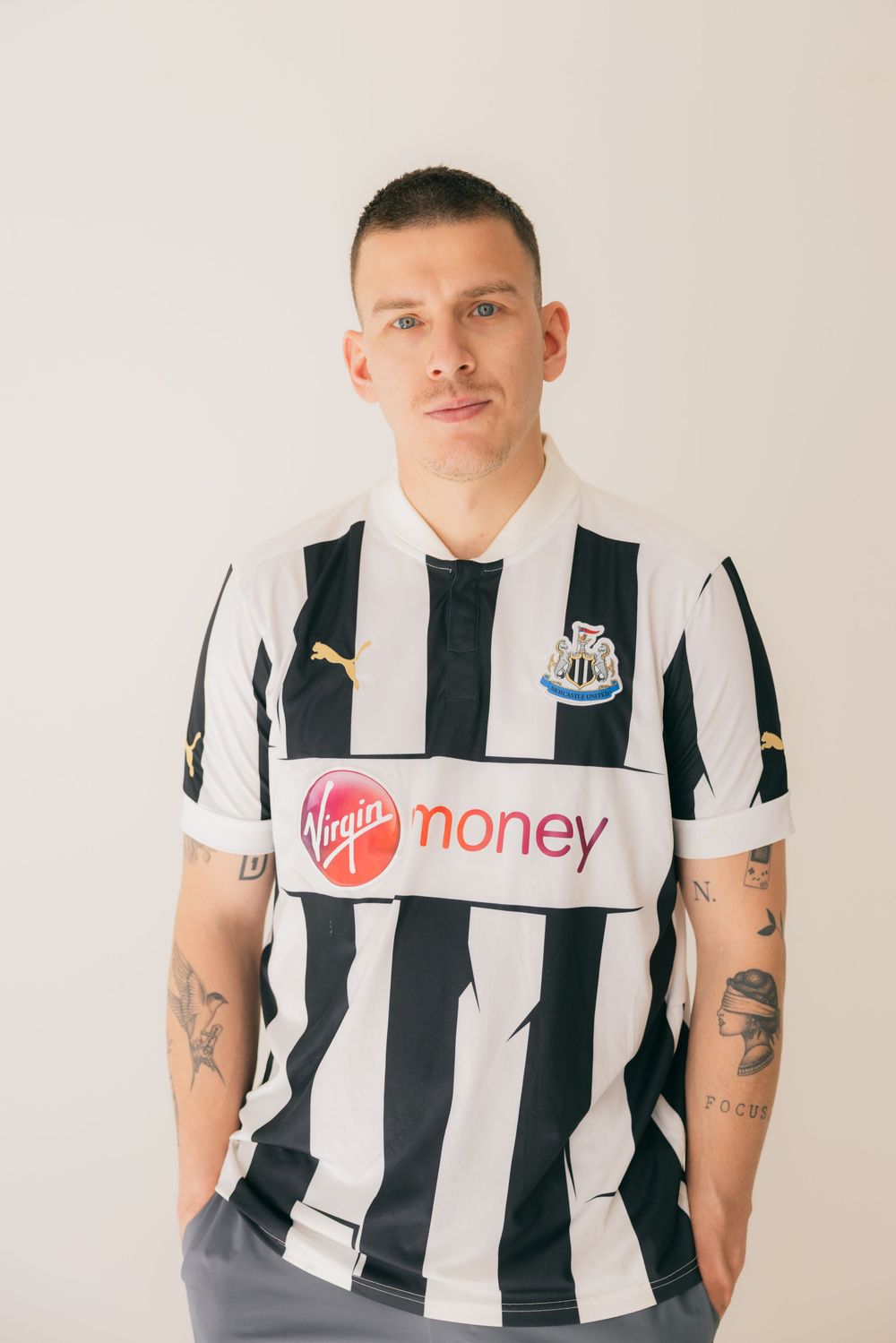 Man wearing Newcastle United black and white striped Puma jersey with Virgin Money sponsor.