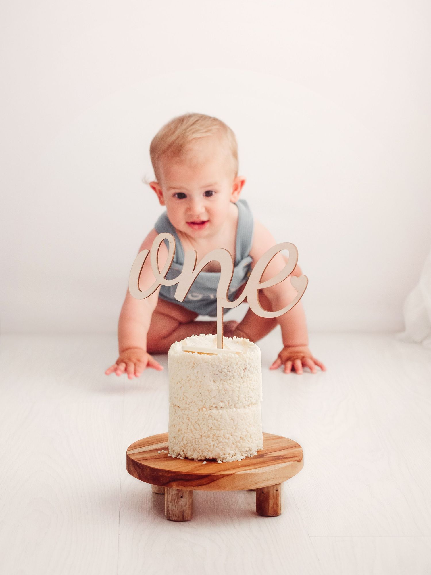 One year old baby boy crawls towards a birthday cake