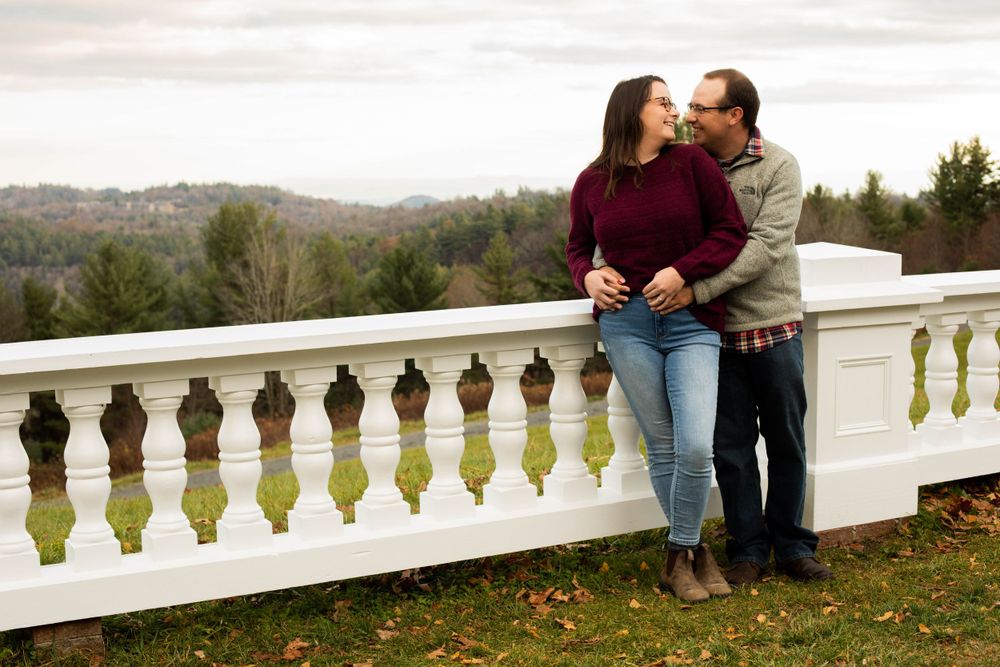 A couple sits together on a white balustrade overlooking an autumn landscape.
