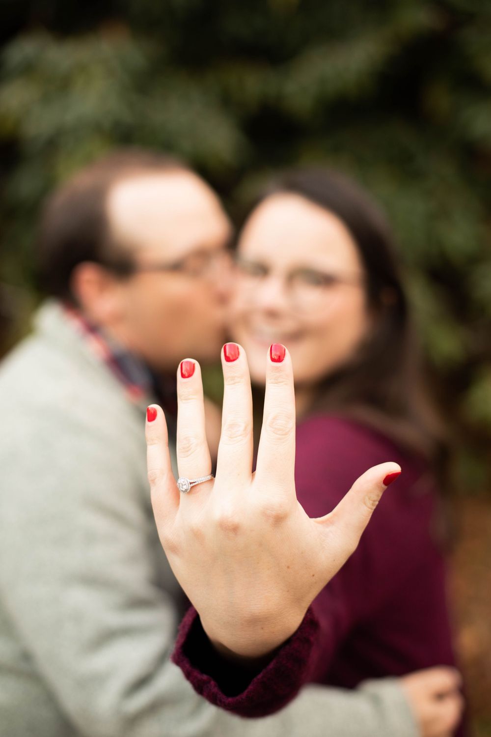 Close-up of a hand with red nail polish showing off an engagement ring.