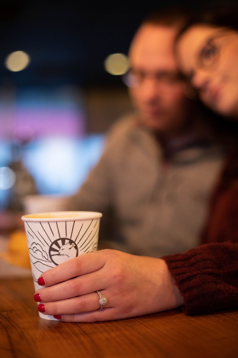 Coffee cup with ring visible on hand with red nail polish.