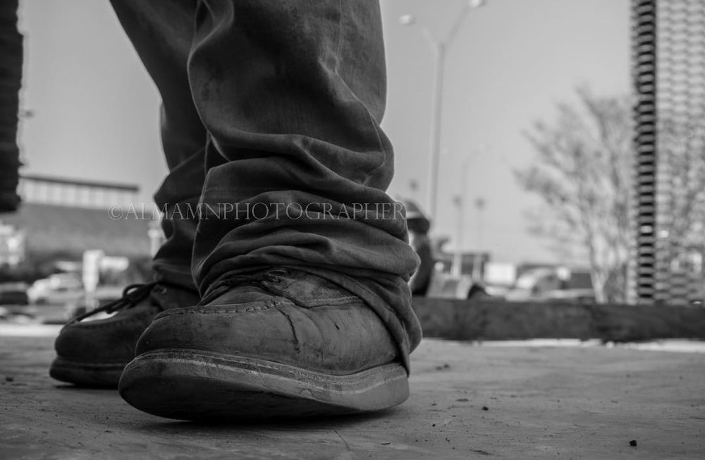 Low angle black and white shot of worn work boots on concrete surface.