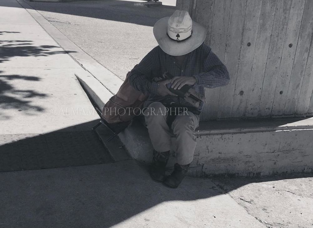 A person in a wide-brimmed hat sits against a wall creating dramatic shadows.