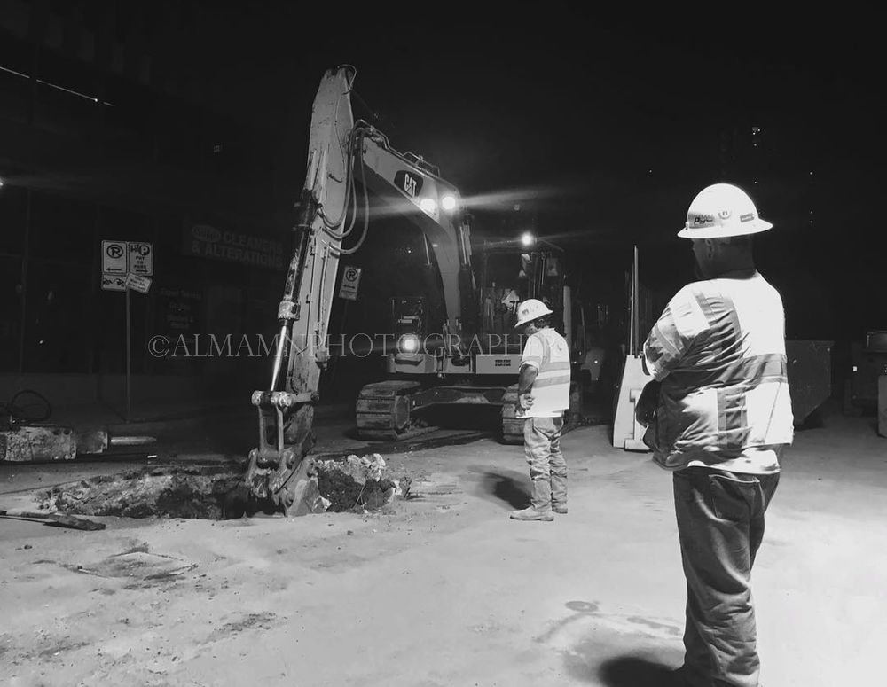 Construction workers observing heavy machinery at night under bright lights.