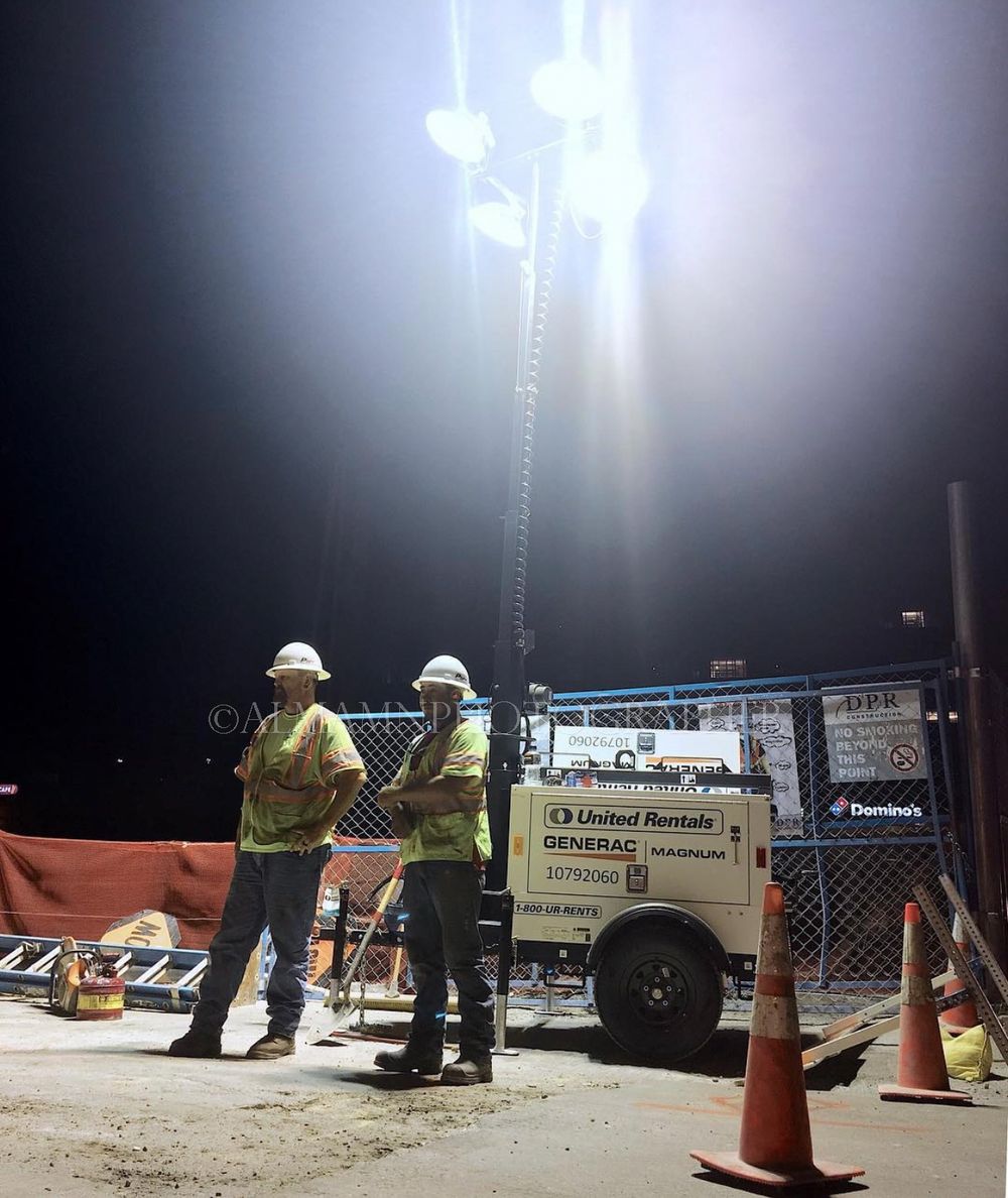 Two workers in safety gear standing near illuminated equipment at a construction site.
