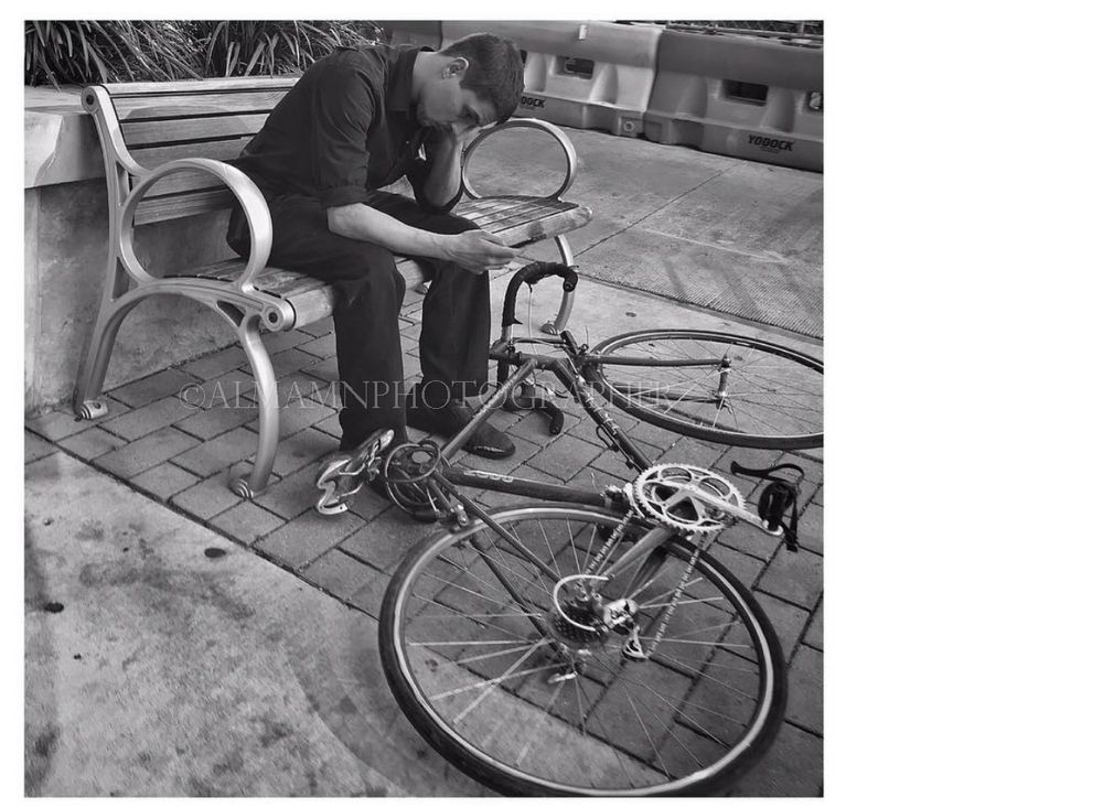 Black and white photo of a bicycle and someone seated on a bench.