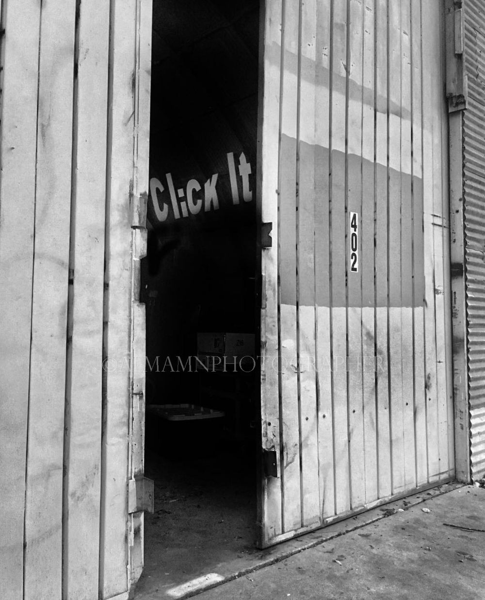 Black and white photo of an open doorway with 'Check In' text visible on wooden planks.