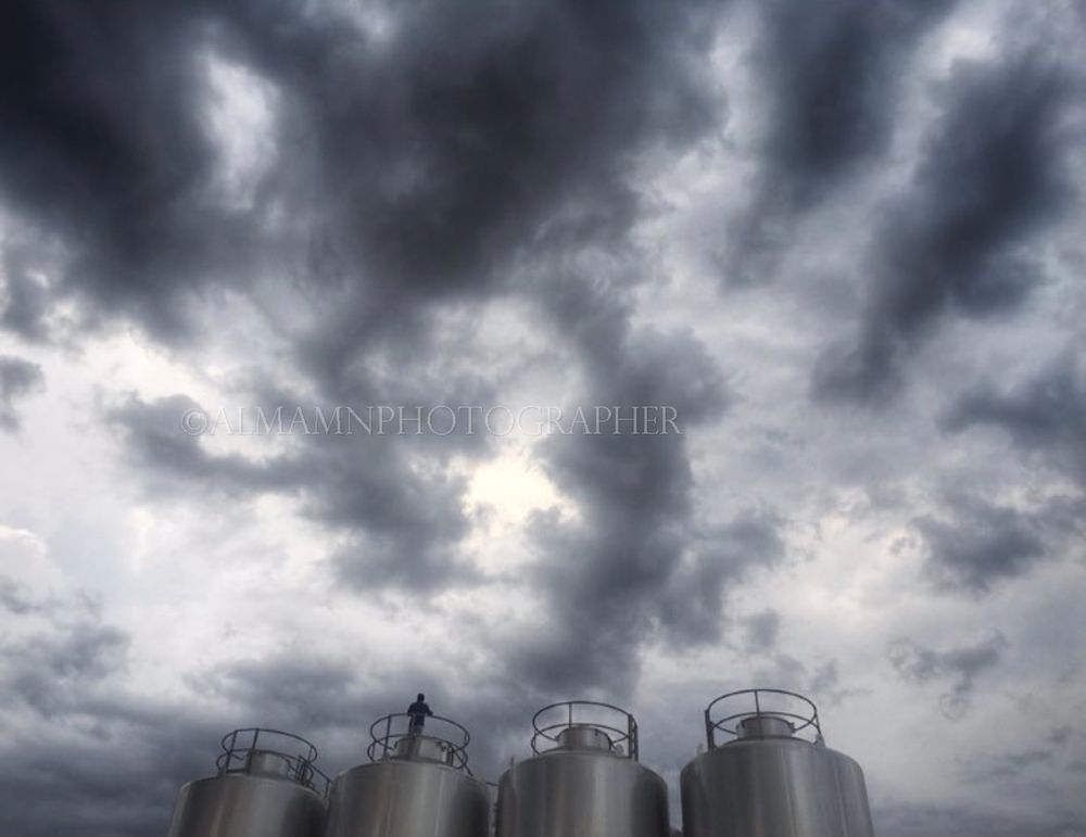 Industrial storage tanks under an ominous stormy sky with dark rolling clouds.