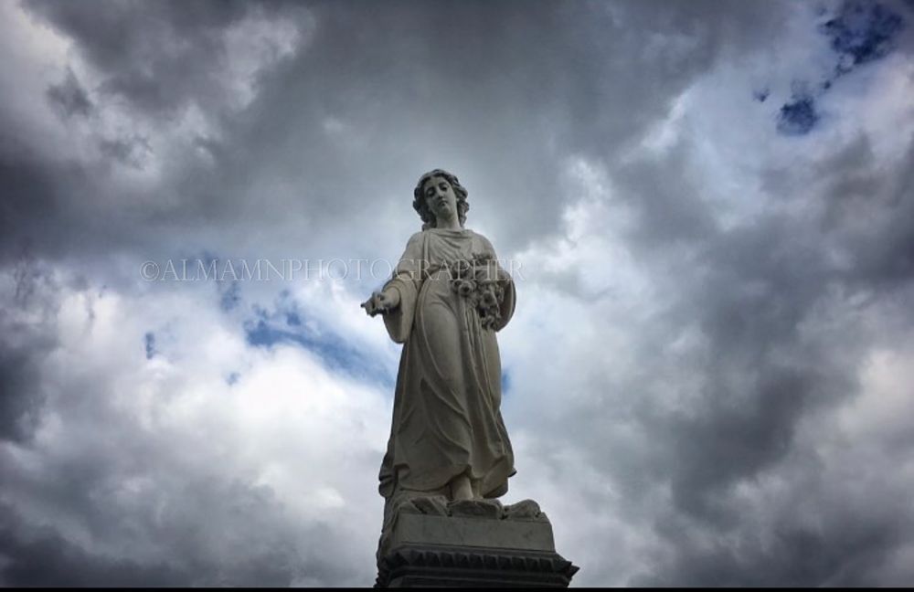 Religious statue silhouetted against dramatic storm clouds in the sky.