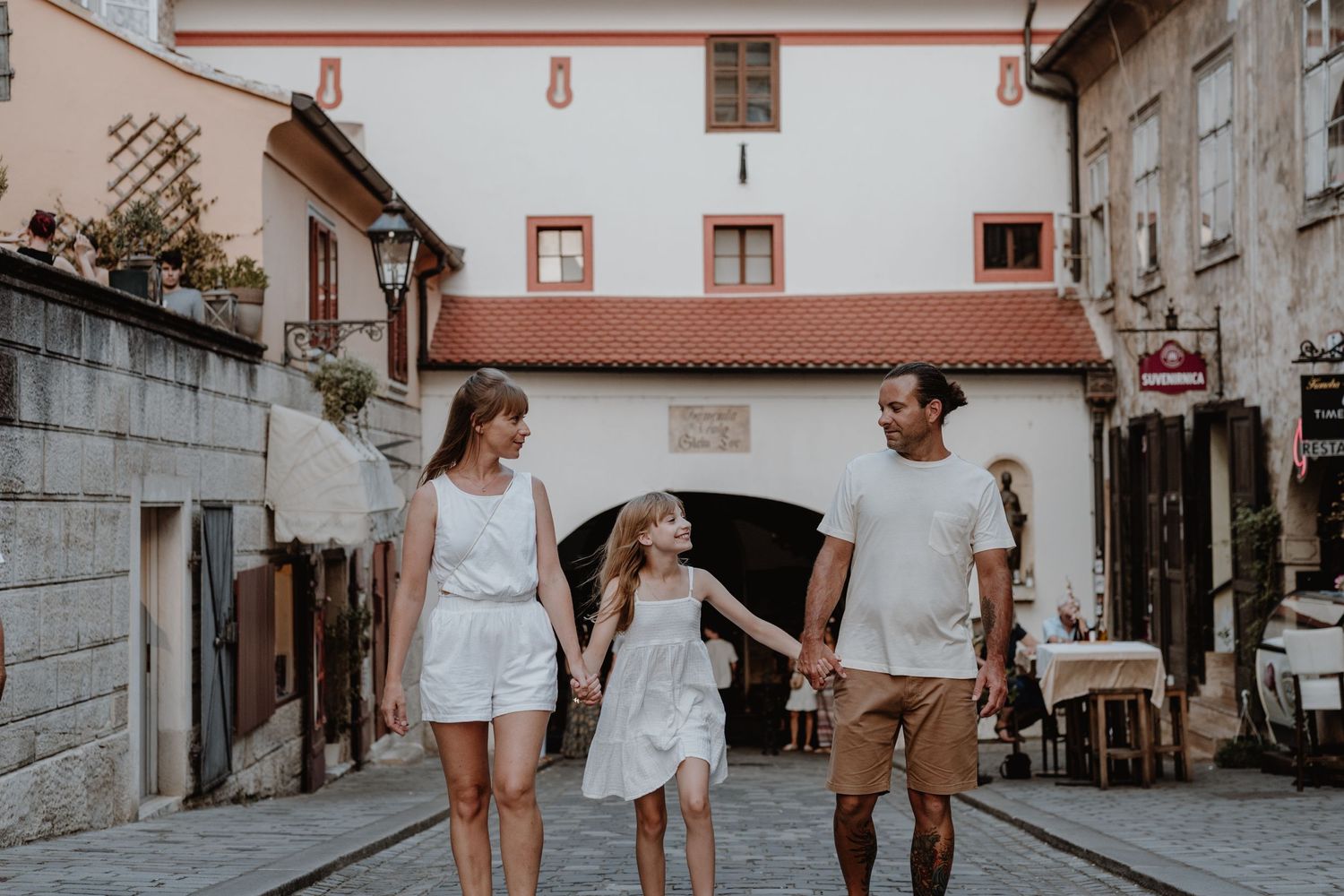 Family walking together through charming old European cobblestone street on summer day.