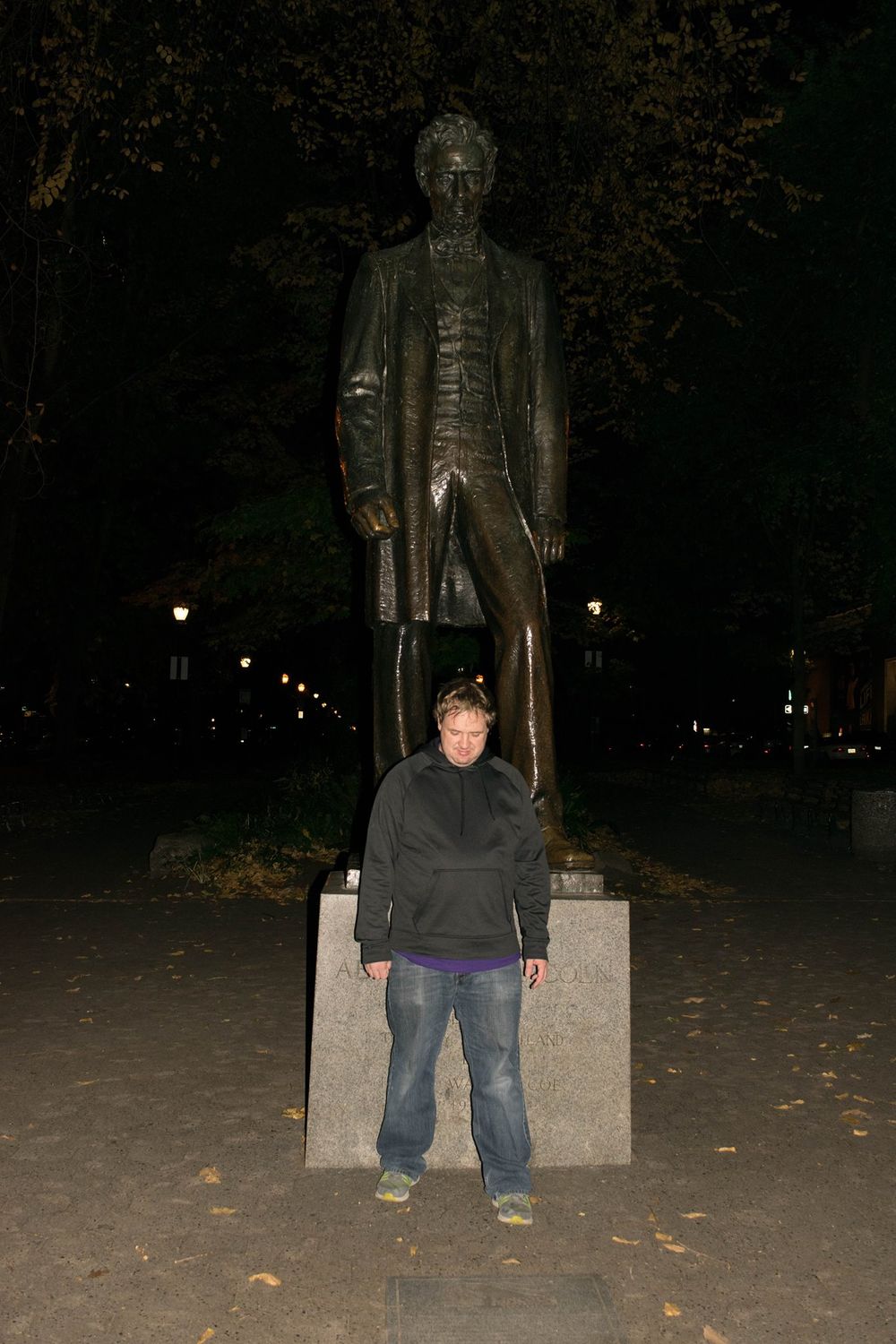 Historic bronze statue stands tall in park setting illuminated by evening lights.