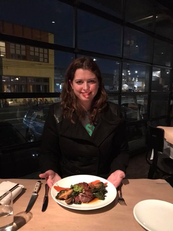 Elegant plated dinner served at upscale restaurant with city lights visible through window.