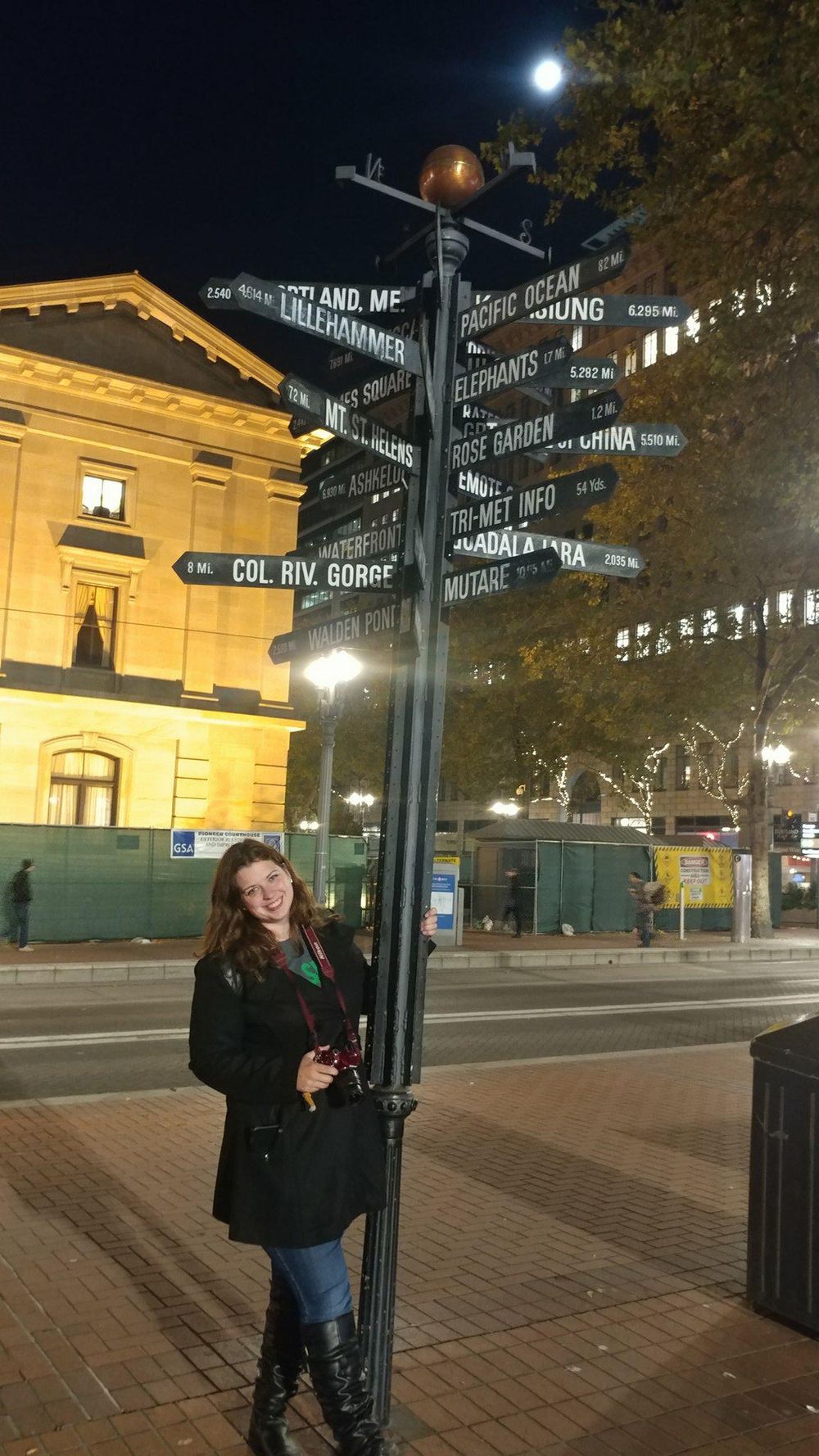 Directional street sign post displaying multiple destinations at night with historic building in background.