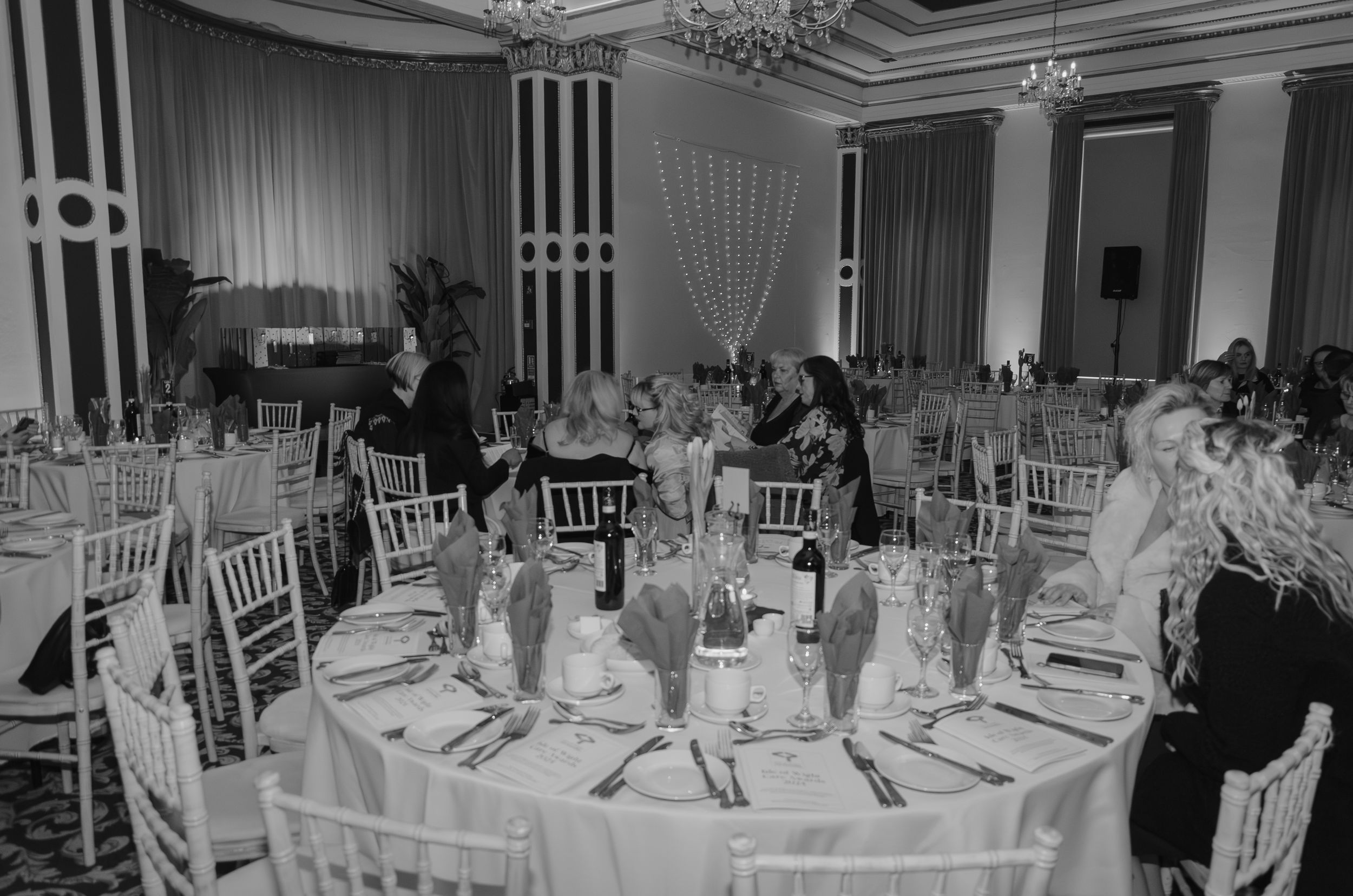 Elegant black and white photo of formal dining room with chandelier and place settings.