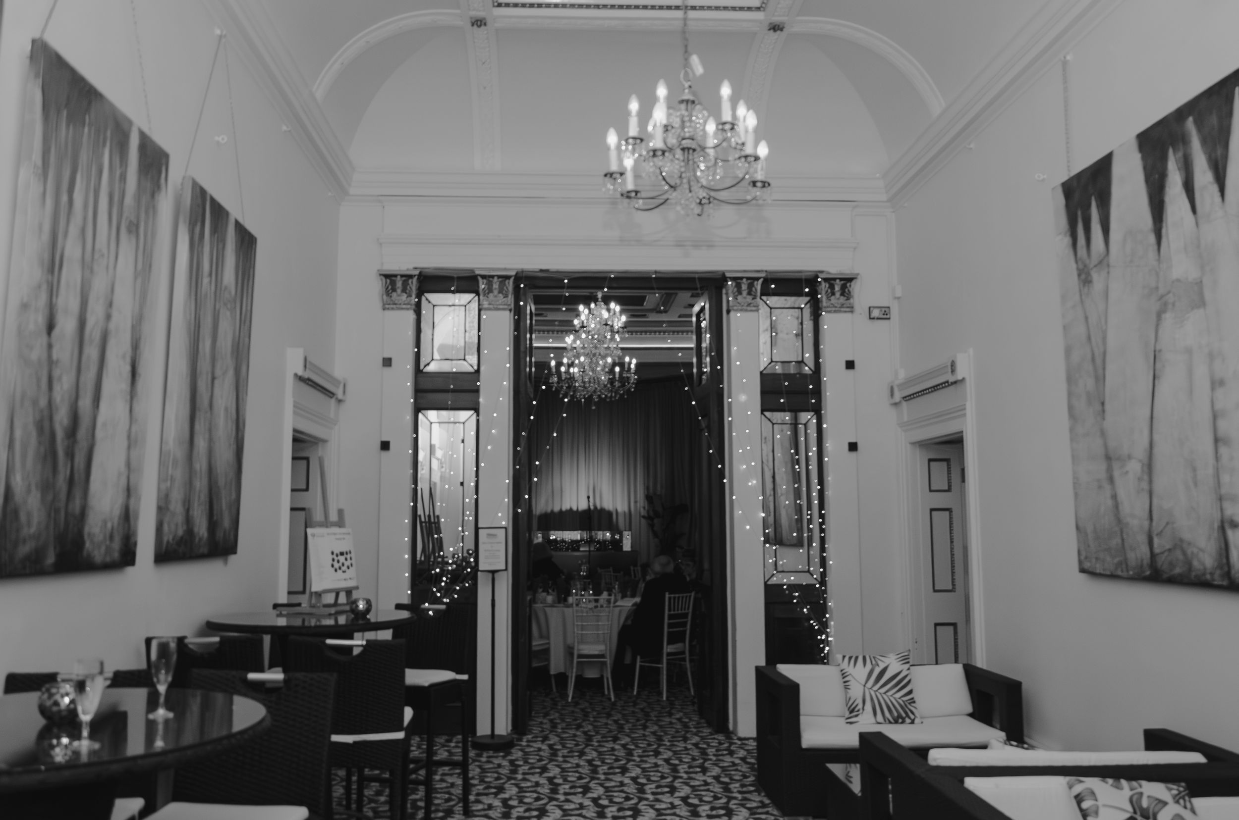 Black and white interior of classic hallway with chandelier and ornate doorway.