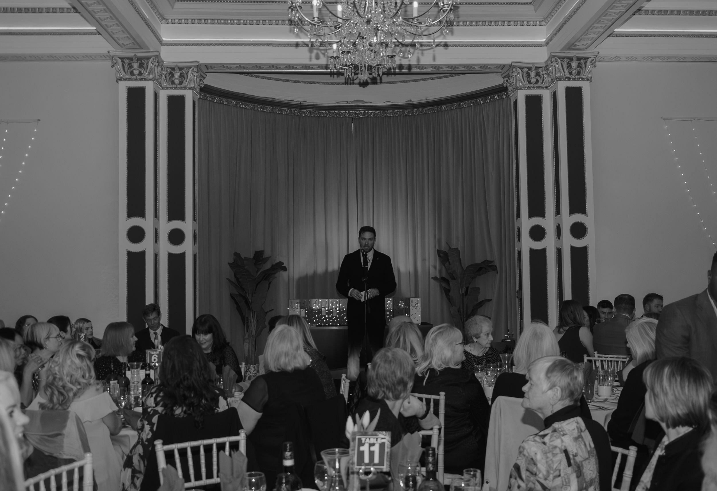 People gathered for a formal event in an ornate ballroom with chandeliers and classic architecture.
