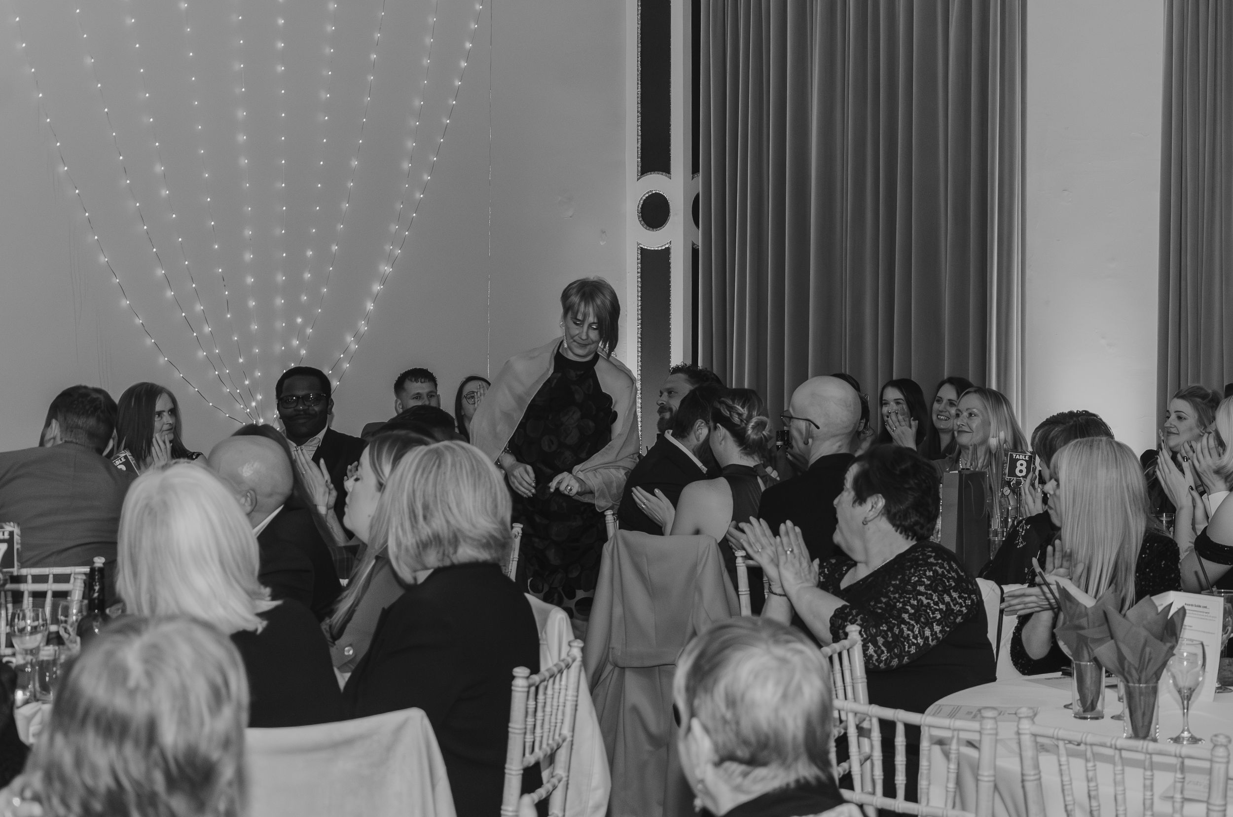 Guests seated at round tables during a formal dinner event with string lights overhead.