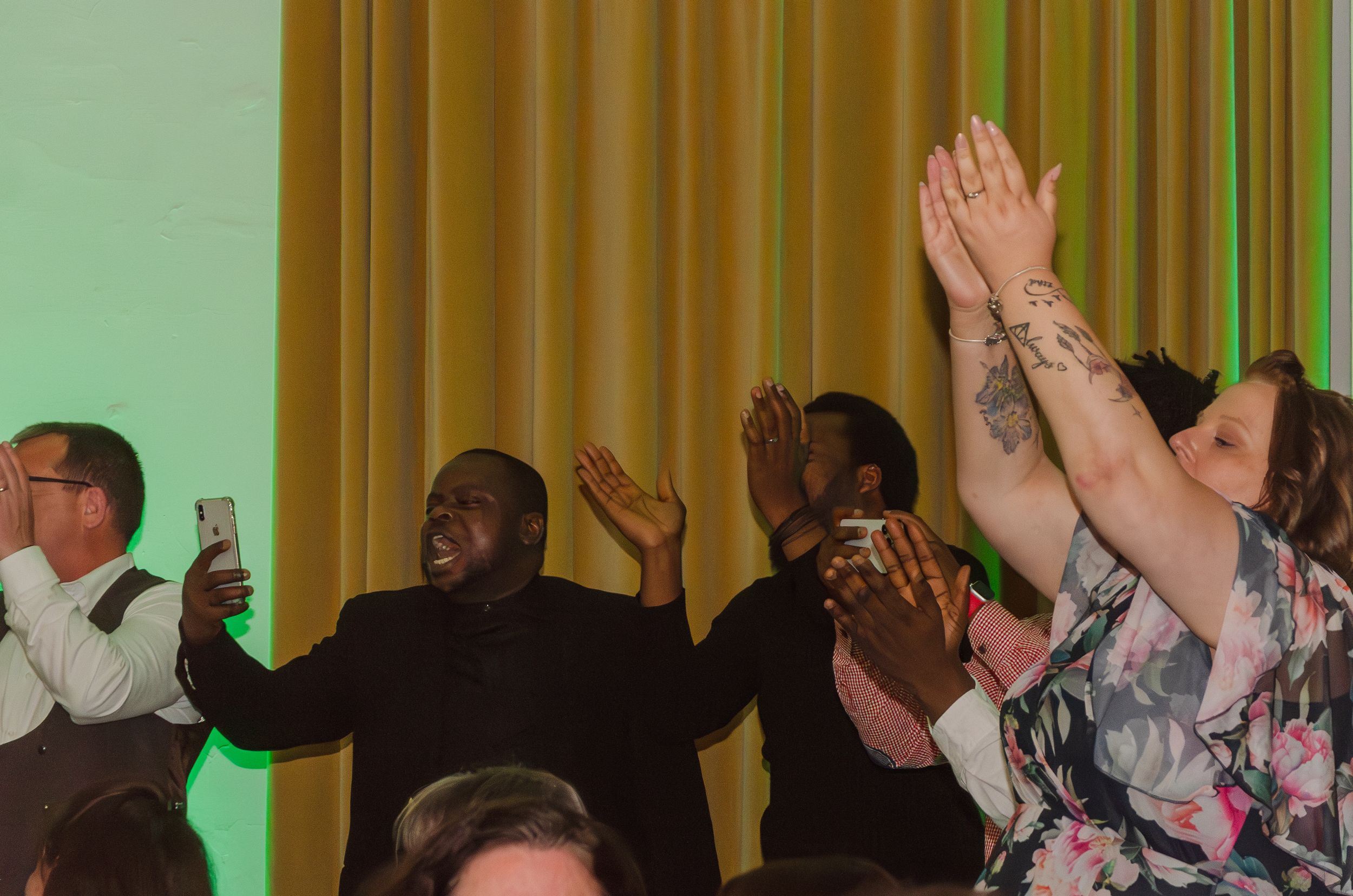A group of people cheering and raising their hands during a celebration with gold curtains.
