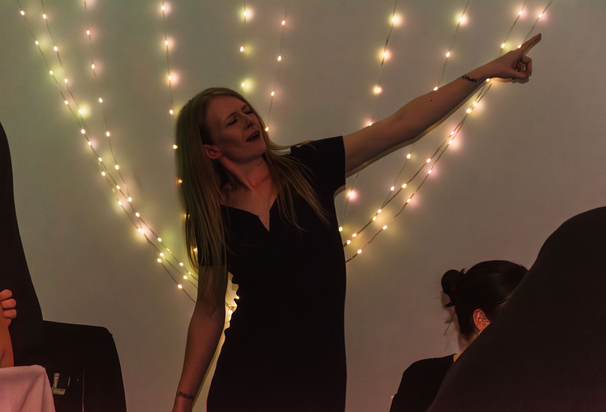 A silhouette of someone dancing with arms raised against a backdrop of twinkling lights.