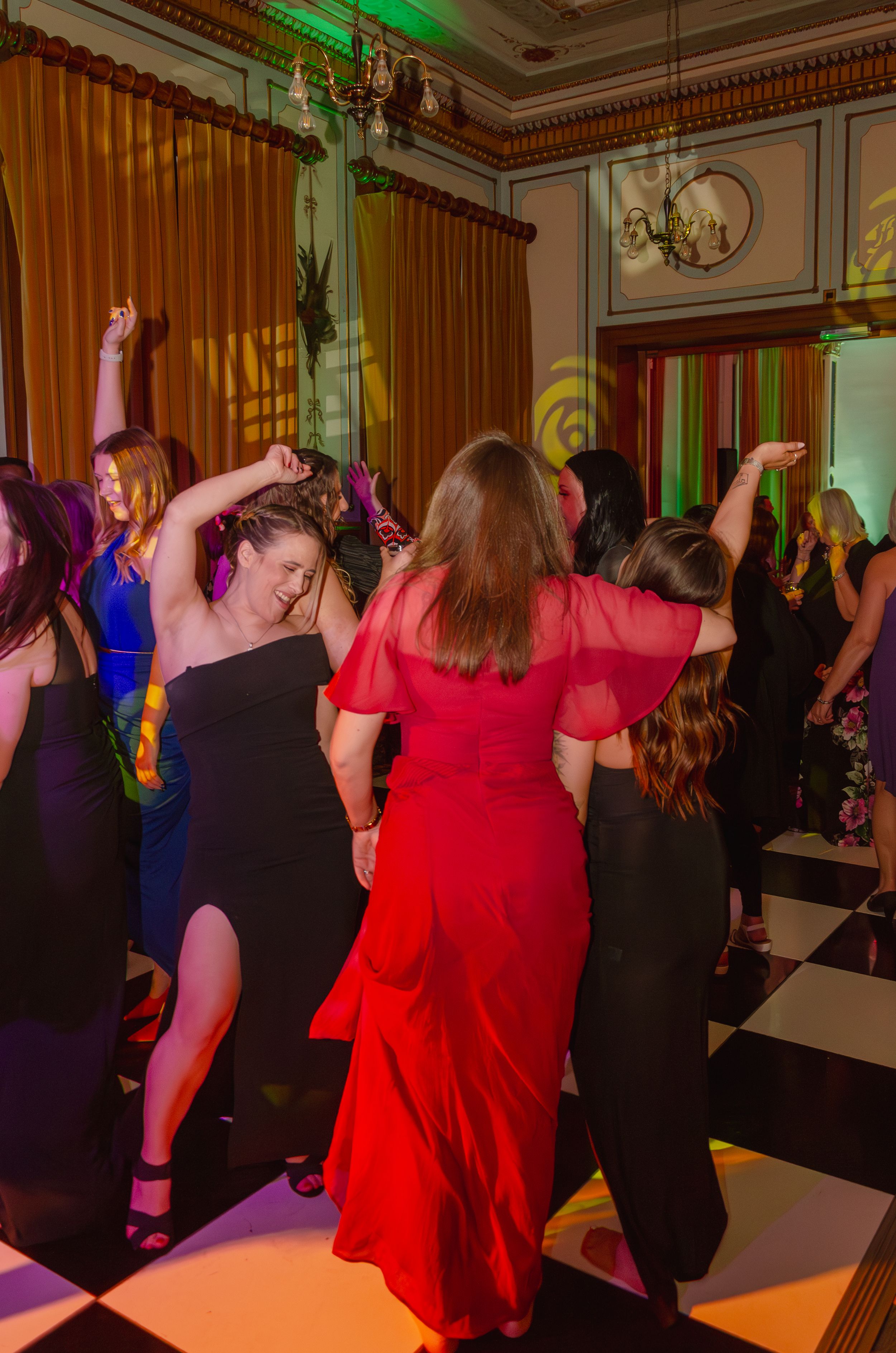 People dancing at a party with colorful lighting and elegant curtains in the background.