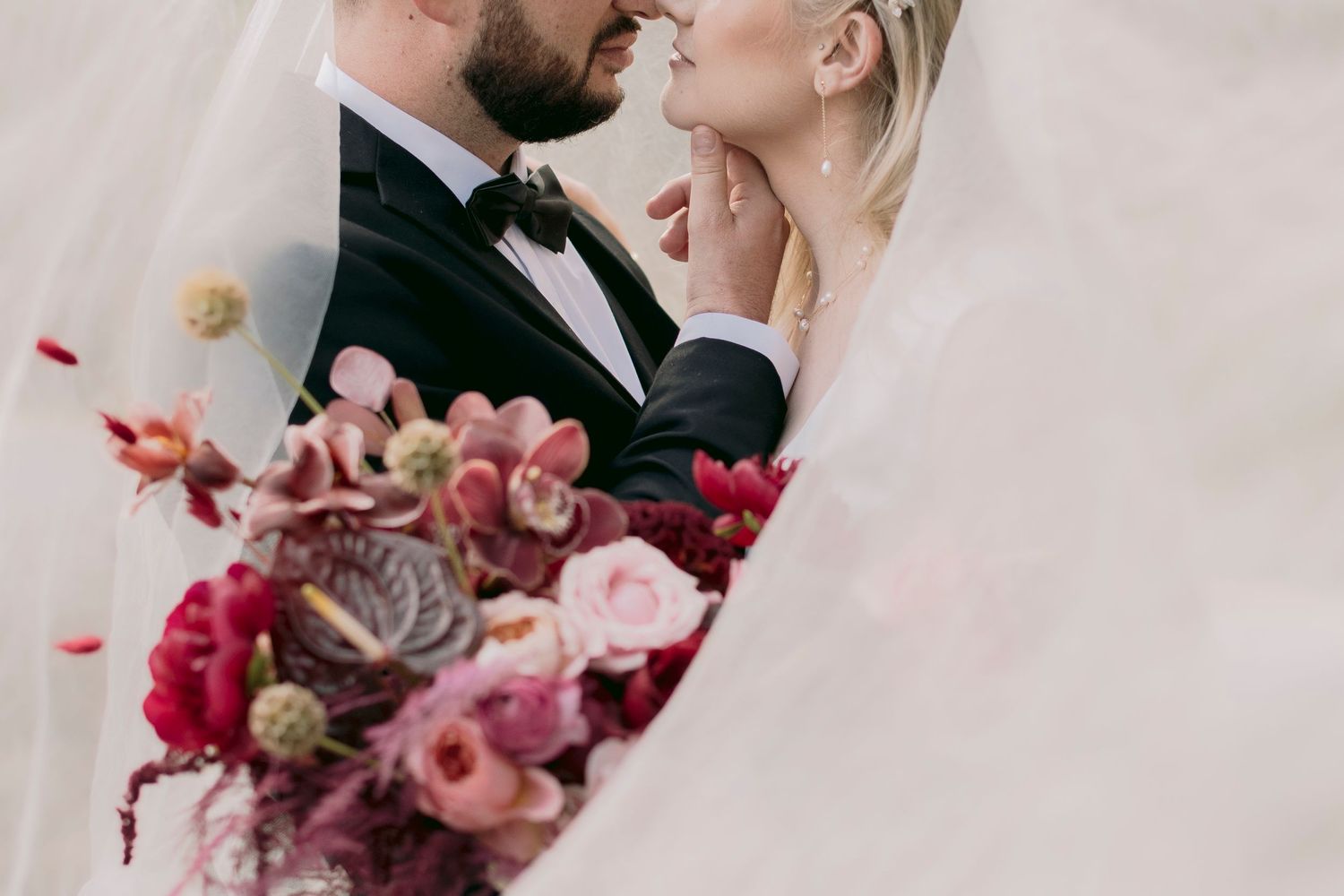Bride and groom nearly kissing framed by a veil with colorful bouquet.