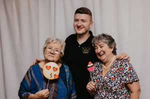 Three generations pose together holding photo booth props and smiling.