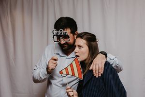 Two people share a laugh while holding props in a photo booth setting.