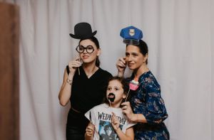 Three people pose playfully with costume props in a photo booth.