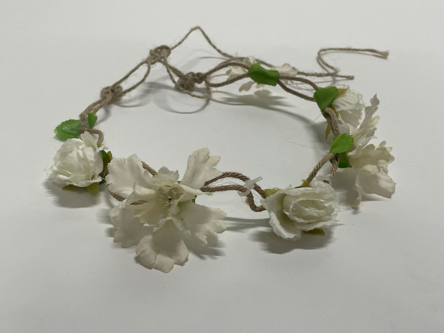White floral headpiece with delicate fabric flowers and green leaves arranged on thin wire.