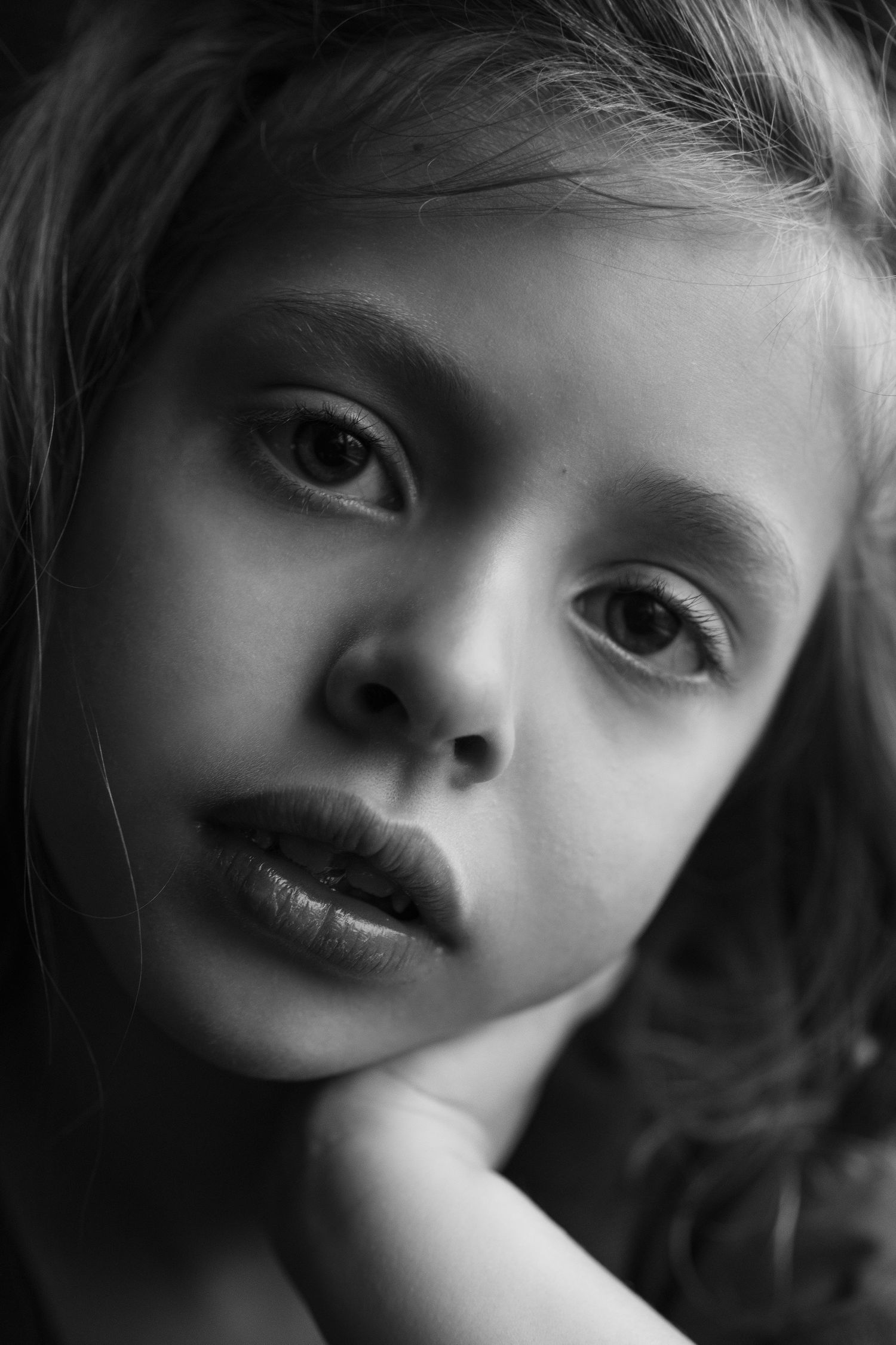 Black and white portrait photograph with dramatic lighting capturing a contemplative expression and soft features.