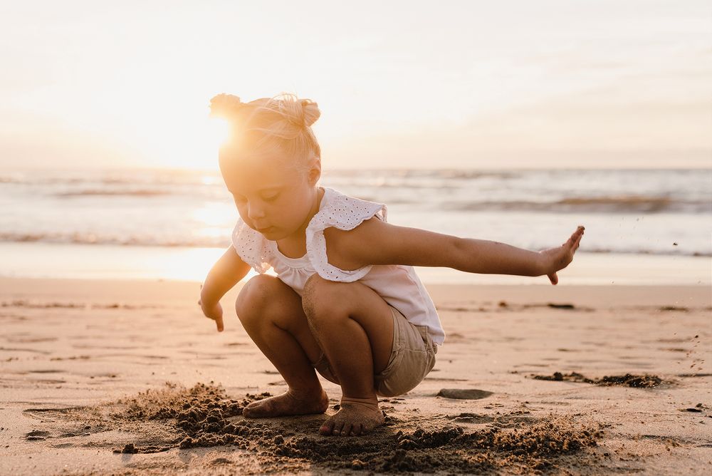 A small child plays in the sand at sunset on a peaceful beach.