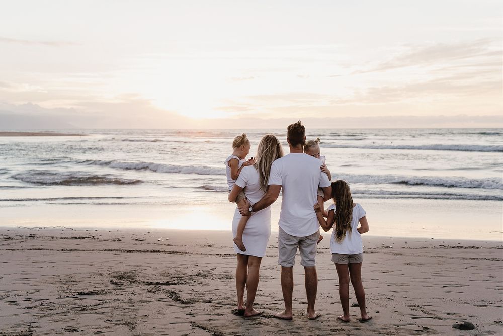 A family stands together watching the sunset over ocean waves on a peaceful beach.