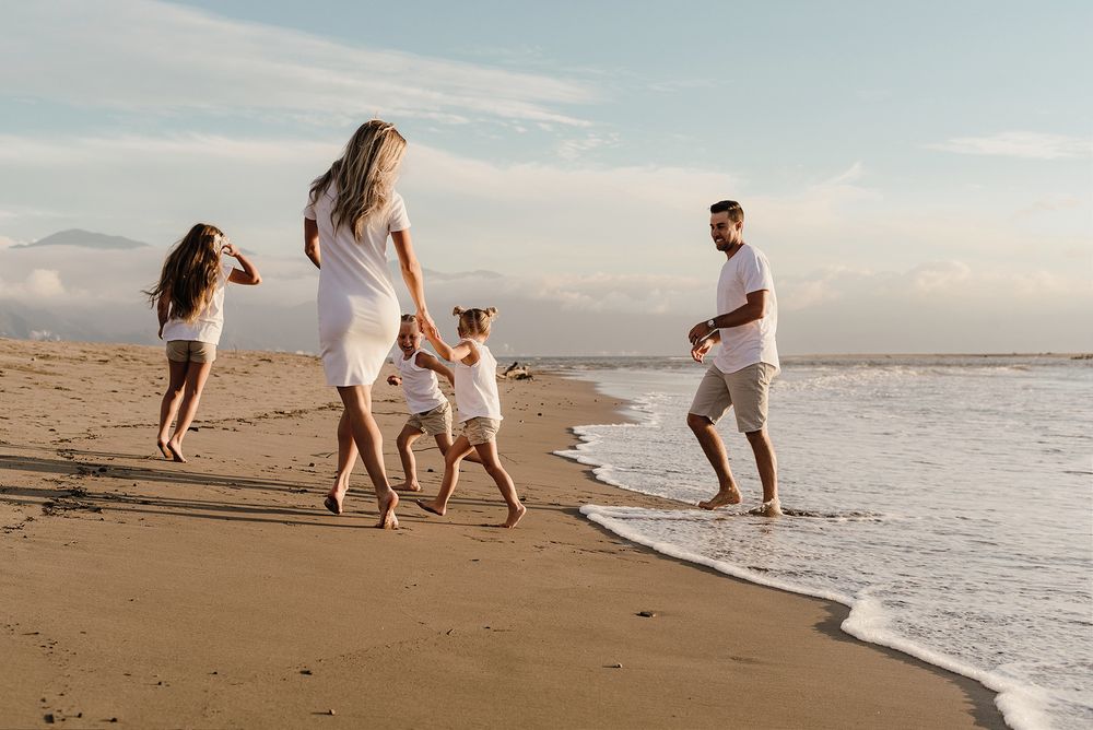 A family walking and playing together along the beach at sunset.