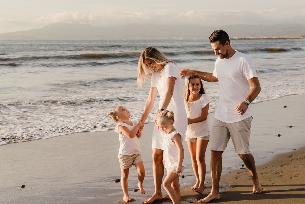 A family dressed in white and beige enjoying a beach walk together at sunset.