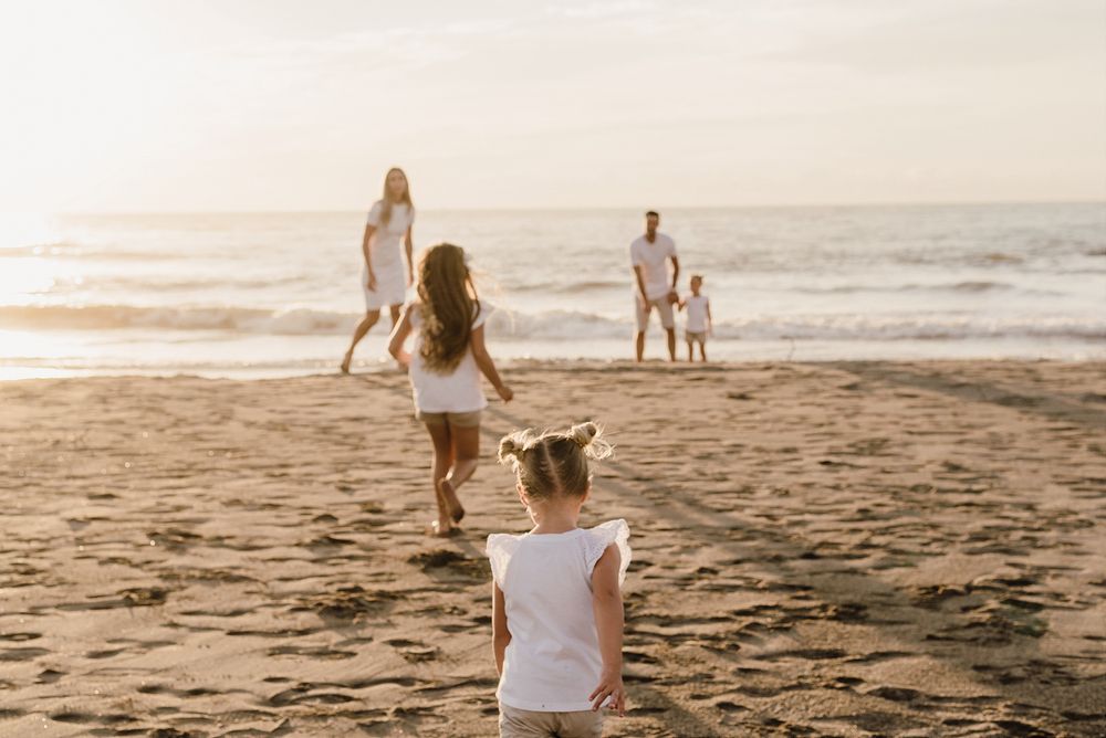 A seaside sunset scene shows people playing and walking along a sandy beach at dusk.