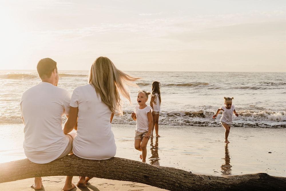 People enjoy a relaxing evening on a beach with driftwood and gentle waves at sunset.