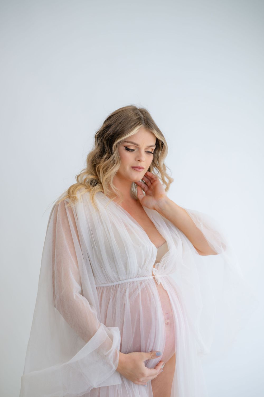 Elegant maternity boudoir photo featuring sheer white flowing dress.