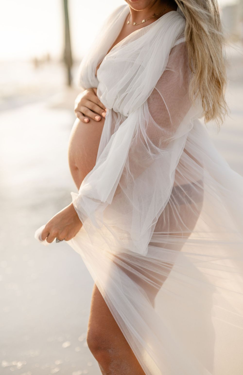 Side view maternity portrait with sheer white fabric flowing in beach breeze.